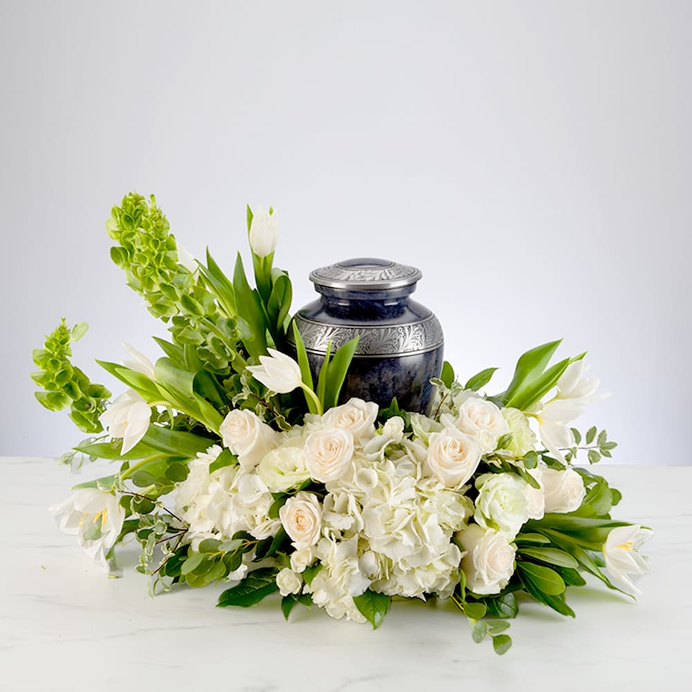 A black urn surrounded by white flowers and green foliage on a white surface. A black urn surrounded by white flowers and green foliage on a white surface.