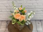 Elegant peach roses and white flowers in a glass vase on a wooden table.