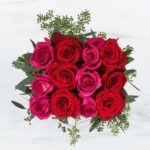 A bouquet of vibrant red and pink roses with greenery.