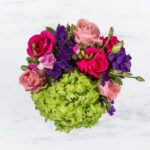 A vibrant bouquet with pink roses, purple flowers, and green hydrangea.