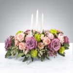 Elegant floral centerpiece with pink and purple roses and three white candles.