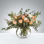 Elegant bouquet of peach roses and eucalyptus in a clear round vase.