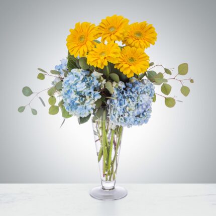 Bright yellow and soft blue flowers arranged in a clear vase.
