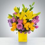 Bright bouquet with yellow lilies and purple roses in a yellow vase.
