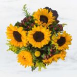 Bright sunflower bouquet with green foliage and red berries.