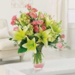 A vibrant bouquet of lilies and roses in a glass vase on a white table.