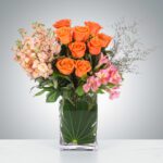 Elegant bouquet of orange roses and mixed flowers in a clear glass vase.