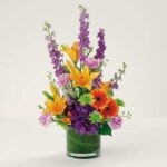 A vibrant bouquet with yellow lilies and purple flowers in a green vase.