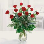A bouquet of red roses in a clear glass vase on a white surface.