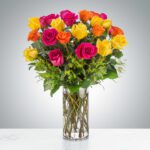 A vibrant bouquet of red, pink, orange, and yellow roses in a clear glass vase.