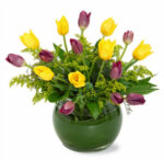 Yellow and purple tulips in a green round vase.