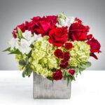 Elegant bouquet of red roses, white lilies, and green hydrangeas in a square vase.