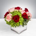 Elegant bouquet of red and pink roses with green accents in a white vase.