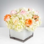 Elegant floral arrangement in a white square vase with roses and hydrangeas.