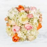 A bouquet of white, peach, and pink roses with hydrangeas.