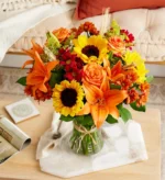 Bright bouquet with sunflowers and orange lilies in a glass vase.