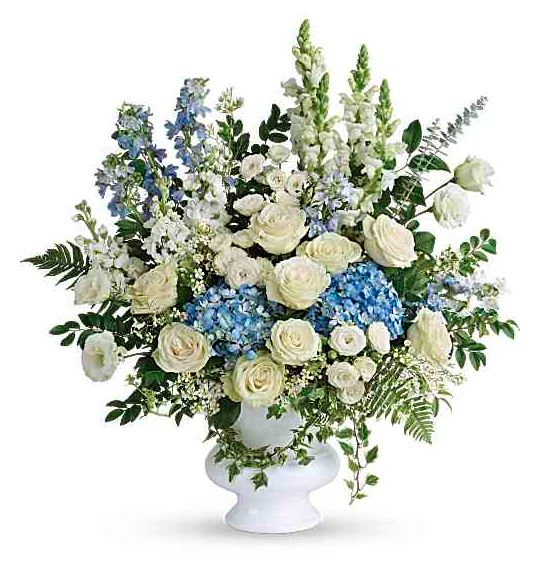 A large, elegant floral arrangement in a white pedestal vase featuring white roses, blue hydrangeas, blue delphiniums, and white snapdragons with lush greenery.