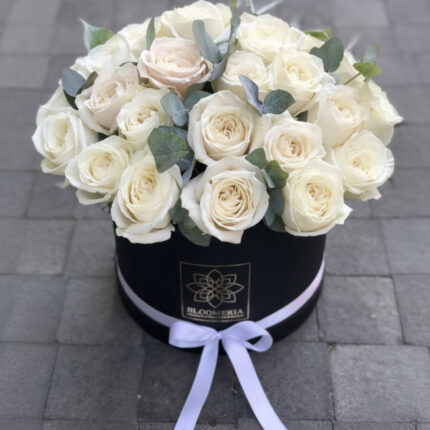 White rose flower box arrangement in a black round hatbox, filled with fresh ivory roses and eucalyptus accents, finished with a white ribbon bow.