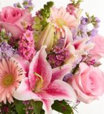 A lush and vibrant floral arrangement featuring a mix of pink Oriental lilies, light pink roses, soft pink gerbera daisies, and lavender stock flowers, accented with green snapdragons and small purple waxflowers.