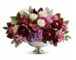 A lush and elegant floral centerpiece in a silver mercury glass pedestal bowl, featuring a rich palette of burgundy dahlias, purple hydrangeas, cream roses, and pink orchids accented with silvery dusty miller leaves.