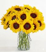 A large, dense bouquet of vibrant yellow sunflowers with dark brown centers, arranged in a clear glass jar wrapped in a black wire mesh or chicken wire.