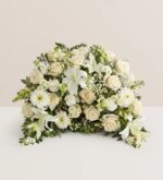 A lush, semi-circular floral arrangement featuring a variety of white and cream-colored flowers including roses, lilies, and chrysanthemums, accented with green foliage.