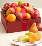 A premium burgundy gift box filled with a variety of fresh fruits including red apples, green and brown pears, and bright oranges, tied with a large red satin ribbon.