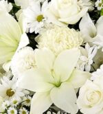 A close-up view of an elegant all-white floral arrangement featuring lilies, roses, carnations, and chrysanthemums.