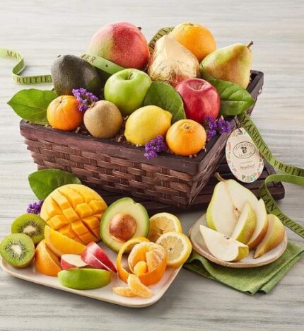 A premium "Manhattan Fruitier" deluxe gift basket filled with assorted fresh fruits including mango, pears, apples, oranges, and kiwi, with some sliced fruit presented on a side plate.
