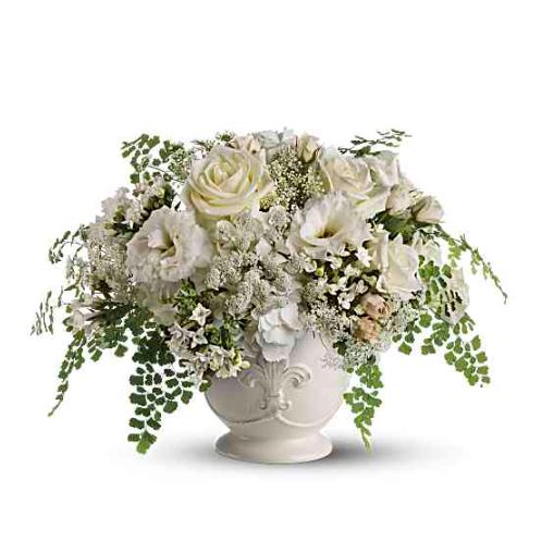 A sophisticated floral centerpiece featuring creamy white roses, lisianthus, and delicate lace flowers accented with cascading green maidenhair ferns, all arranged in a vintage-style white ceramic pedestal vase with embossed detailing.