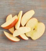 Slices of a fresh red apple and one large cross-section slice arranged on a gray wooden surface.