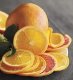 A vibrant close-up of fresh orange and grapefruit slices arranged artistically on a dark surface, with a whole citrus fruit and green leaves in the background.