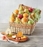 A premium organic fruit gift basket overflowing with fresh pears, oranges, and apples, presented in a woven wicker basket with a wooden cutting board featuring sliced fruit in the foreground.