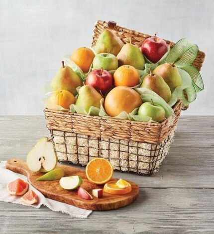 A premium organic fruit gift basket overflowing with fresh pears, oranges, and apples, presented in a woven wicker basket with a wooden cutting board featuring sliced fruit in the foreground.