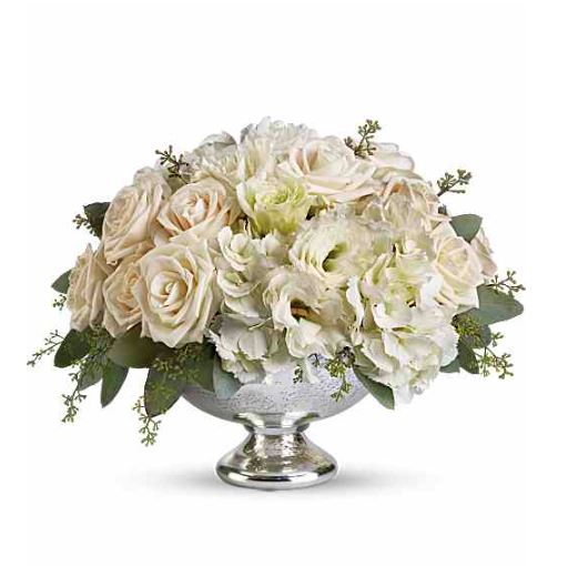 A luxurious floral centerpiece featuring cream and white roses, carnations, and hydrangeas in a silver mercury glass pedestal bowl.