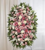 A large, elegant funeral standing spray featuring a dense arrangement of pink roses, white lilies, stargazer lilies, and white chrysanthemums set against lush green palm leaves.
