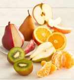 A vibrant assortment of sliced and whole fresh fruits including red and bosc pears, kiwi halves, orange slices, a peeled mandarin, and apple segments arranged on a white wooden surface.