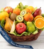 A large, woven brown wicker basket overflowing with a variety of fresh fruits including apples, pears, oranges, and kiwis, set against a white wooden background.