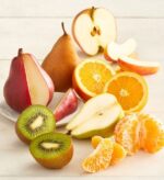 A variety of fresh, sliced and whole fruits including red and green pears, oranges, apples, kiwi, and a peeled mandarin orange arranged on a light-colored wooden surface.