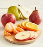 A fresh fruit arrangement featuring a whole red apple, a green pear, a red pear, and sliced pieces of orange, apple, and a peeled mandarin orange on a wooden board.