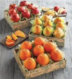 Three premium gift boxes from Harry & David filled with fresh red apples, Royal Riviera pears (one gold-wrapped), and bright oranges, accompanied by sliced fruit on wooden platters.