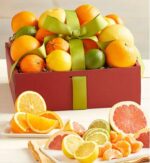 A premium "Welcome Sunshine" gift box filled with an assortment of fresh citrus fruits including oranges, grapefruits, lemons, and limes, tied with a decorative green ribbon. Sliced citrus pieces are displayed in the foreground.
