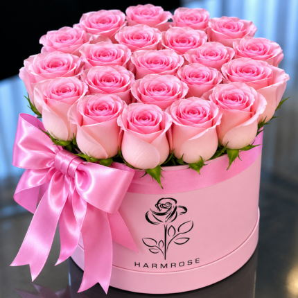 A luxurious circular pink gift box filled with fresh, light pink roses, decorated with a matching satin pink ribbon and bow.