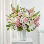 A lush floral arrangement featuring white lilies, pink roses, pink carnations, and white daisies in a white ceramic vase.