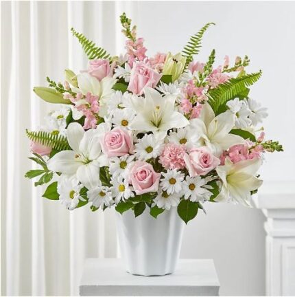 A lush floral arrangement featuring pink roses, white lilies, and white daisies in a white ceramic vase.